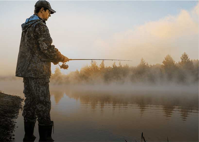 Person fishing at misty lake during sunrise.
