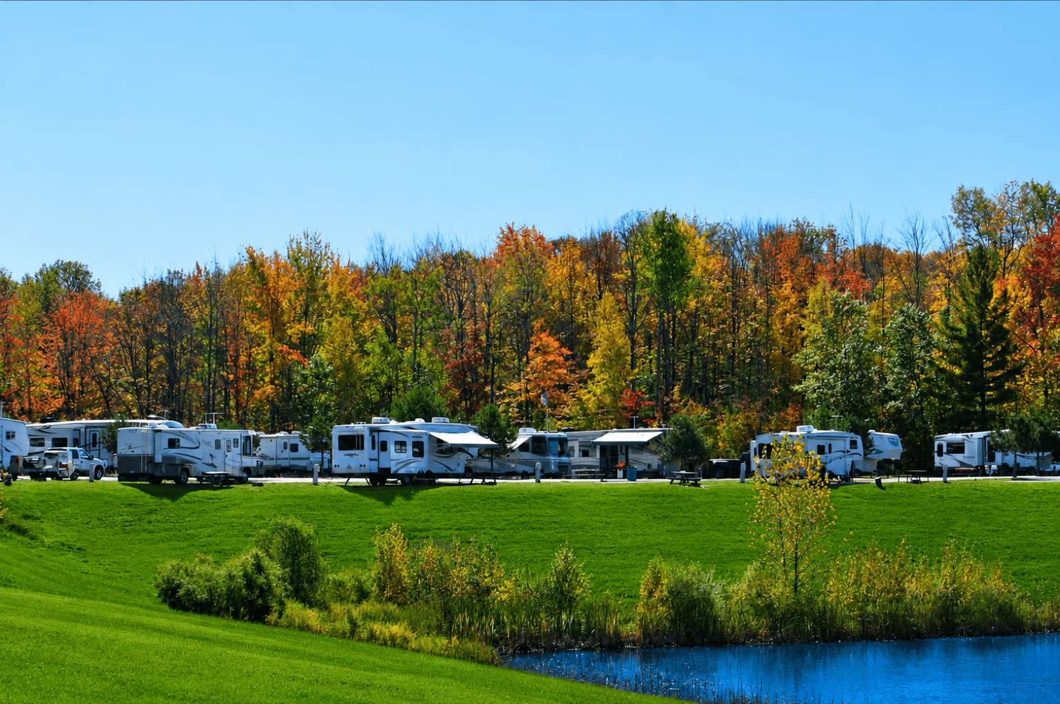 RVs parked by pond with autumn trees