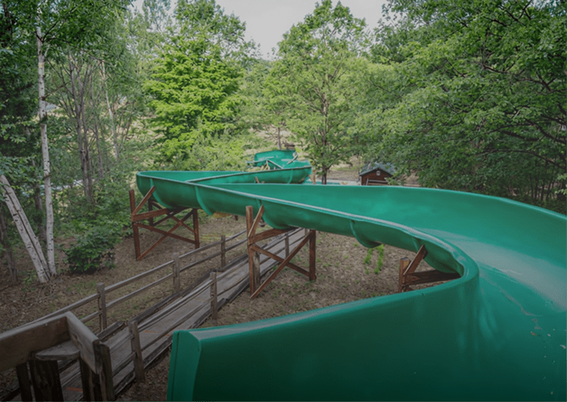 Green outdoor waterslide surrounded by trees.