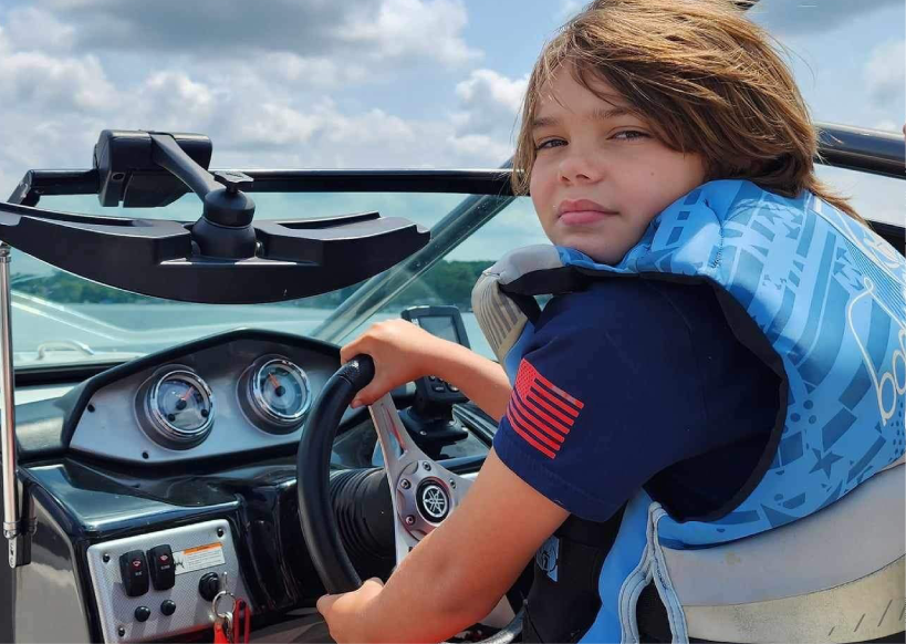 Child steering motorboat wearing blue life jacket